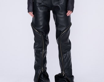 Op de afbeelding: Zwarte leren broek met meerdere ritsdetails. De broek heeft een hoge taille en is nauwsluitend langs de benen. De ritsen lopen langs de zijkanten van de benen en eindigen bij de enkels.
