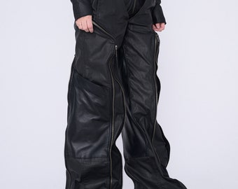 Op de afbeelding: Zwarte leren broek met meerdere ritsen langs de benen. De broek heeft een wijde pijp en een hoge taille.