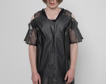 Op de afbeelding: Een zwart, lang mouwig shirt met een knoopsluiting en een transparante overlay. Het shirt heeft een v-hals en uitgesneden schouders.