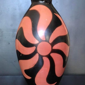 Puede incluir: Un jarrón de cerámica negro con un diseño estilizado de sol naranja.