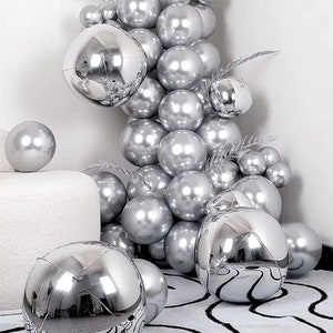 May include: A silver balloon arch with a variety of sizes and shapes. The balloons are shiny and reflect light. The arch is decorated with greenery.