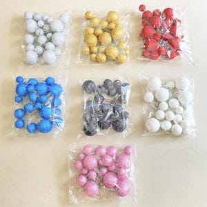 May include: Assortment of 10 packs of decorative foam balls with wire stems. The balls are in various colors, including silver, gold, red, blue, black, white, and pink.