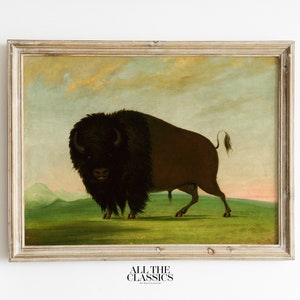 May include: A framed painting of a brown bison standing in a grassy field with a mountain range in the background. The sky is a light blue with a few clouds. The painting is in a simple wooden frame.