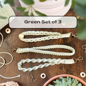 May include: A set of three green macrame keychains with wooden beads and metal clasps. The keychains are displayed on a wooden surface with green plants in the background. Green Set of 3.