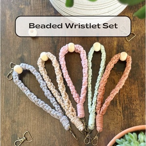 May include: Set of five beaded wristlets in various pastel colors, including light blue, pink, beige, and green. Each wristlet has a wooden bead and a gold-toned metal clasp.