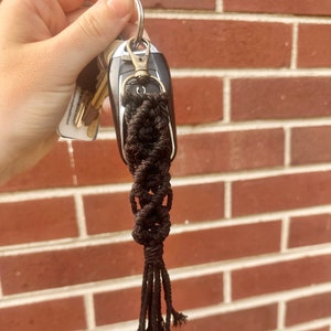 May include: A black macrame keychain with a tassel hanging from a silver key ring.