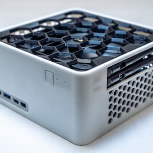 Könnte beinhalten: Ein weißer, würfelförmiger Computer mit einem schwarzen Wabengitter auf der Oberseite und der Seite. Der Computer hat zwei schwarze Antennen, die sich von der Oberseite erstrecken.