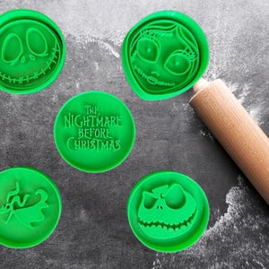 May include: Green cookie cutters featuring characters from "The Nightmare Before Christmas" and a wooden rolling pin. The cutters include Jack Skellington, Sally, and Zero designs, along with a cutter with the movie title.