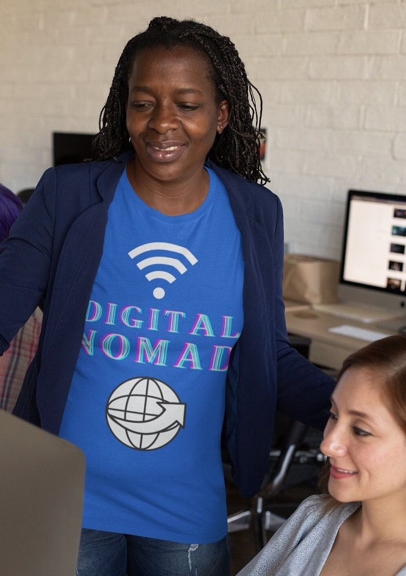 May include: A woman wearing a blue t-shirt with a white wifi symbol, the text "DIGITAL NOMAD" in pink and blue, and a white globe with an arrow. She is wearing a navy blue blazer and blue jeans.