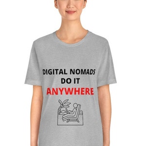 May include: A gray t-shirt with the text "DIGITAL NOMADS DO IT ANYWHERE" in black and red. The shirt features a black and white illustration of a person sitting on a beach chair with a laptop, palm tree, and ocean waves.