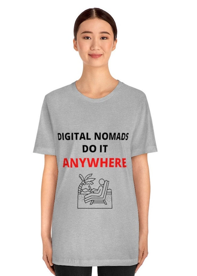 May include: A gray t-shirt with the text "DIGITAL NOMADS DO IT ANYWHERE" in black and red. The shirt features a black and white illustration of a person sitting on a beach chair with a laptop, palm tree, and ocean waves.