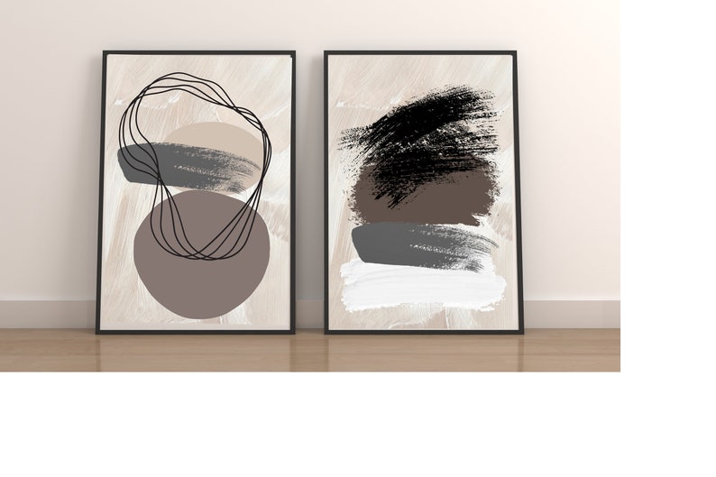 May include: Two framed abstract art prints with a beige background. The print on the left features a brown circle with black lines and a gray brushstroke. The print on the right features a black brushstroke, a brown brushstroke, a gray brushstroke, and a white brushstroke.