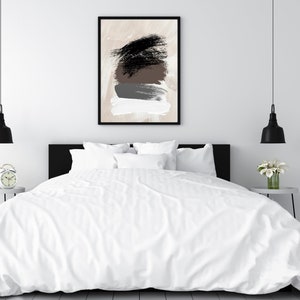 May include: A white bed with a white duvet cover and black headboard. Two black pendant lights hang above the bed. A framed abstract painting with brown, black, and gray brushstrokes hangs on the wall behind the bed.