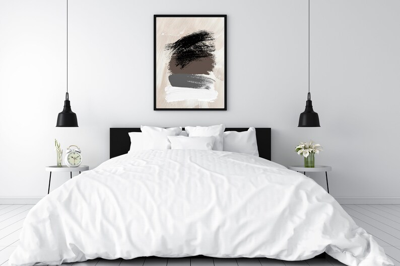 May include: A white bed with a white duvet cover and black headboard. Two black pendant lights hang above the bed. A framed abstract painting with brown, black, and gray brushstrokes hangs on the wall behind the bed.