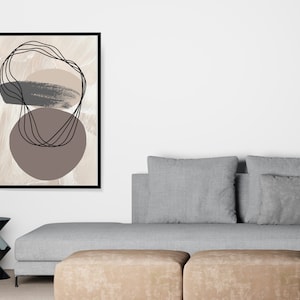 May include: Abstract art print with brown, beige, and black shapes on a beige background. The print is framed in black and is hanging on a white wall above a gray couch.