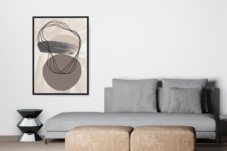 May include: Abstract art print with brown, beige, and black shapes on a beige background. The print is framed in black and is hanging on a white wall above a gray couch.