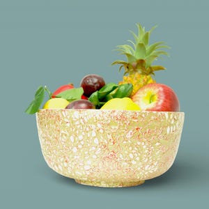 Puede incluir: Un cuenco decorativo lleno de fruta fresca, incluyendo una piña, una manzana roja, ciruelas y limones. El cuenco tiene un patrón floral beige y rojo texturizado. El arreglo está sobre un fondo verde azulado.