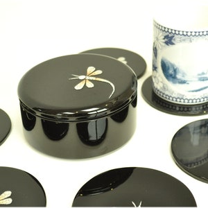 Puede incluir: Un juego de seis posavasos negros con un diseño de libélula. Los posavasos están hechos de madera lacada y tienen un acabado brillante. También se incluye una caja negra lacada con un diseño de libélula.