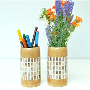 May include: Two bamboo vases with a mosaic design. One vase holds colorful markers and the other holds a bouquet of lavender and orange flowers.