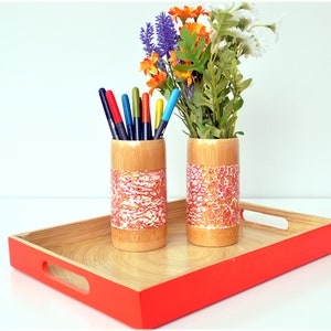 May include: A bamboo tray with a bright orange border holds two bamboo containers. One container holds colorful pens, the other holds flowers. The containers have a decorative band of red and white patterned paper.