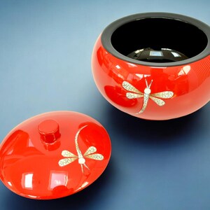 Puede incluir: Tazón de madera lacado en rojo con interior negro y diseño de libélula. El tazón tiene una tapa a juego.