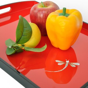 May include: A red serving tray with a black trim, holding a red apple, a yellow bell pepper, and a lemon with green leaves. A dragonfly design is on the tray's surface. The tray has two handle cutouts.