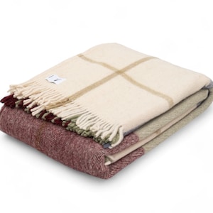 May include: A folded cream, green, and burgundy plaid throw blanket with fringe. The blanket is made of wool and has a soft, cozy texture.