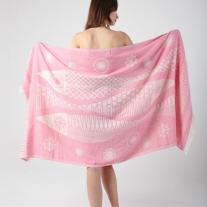 May include: A pink beach towel with a white geometric pattern of fish and stars. The towel is draped over a person's shoulders.