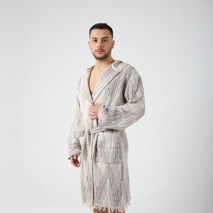 May include: A hooded robe with a geometric pattern in shades of gray and white. The robe has a sash tie and a frayed hem.