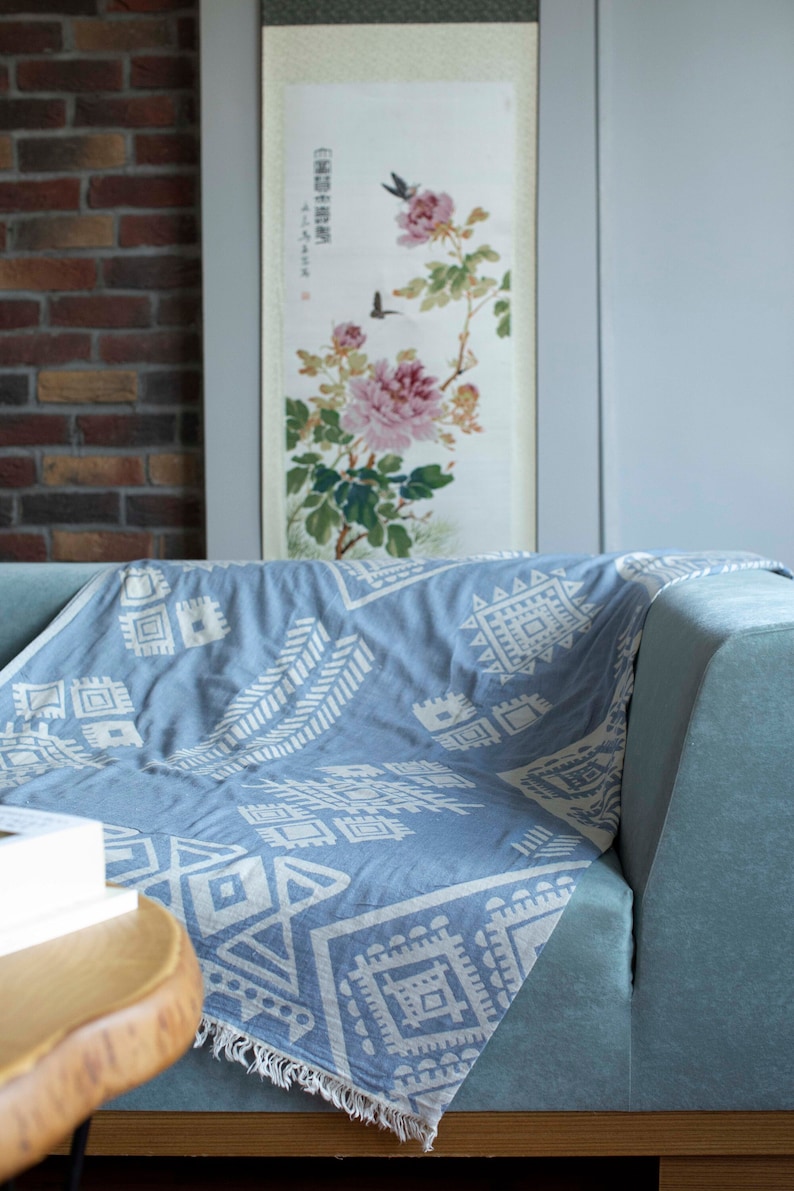 May include: A light blue throw blanket with a white geometric pattern. The blanket is draped over a light blue sofa.