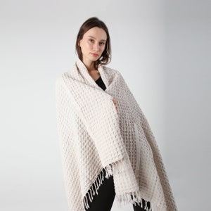May include: A white waffle weave throw blanket with fringe. The blanket is draped over a person's shoulders.