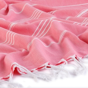May include: A pink and white striped Turkish towel with white fringe. The towel is made of cotton and is soft and absorbent.