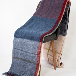 May include: A plaid throw blanket in shades of burgundy, blue, and beige with fringe edges draped over a wooden chair.