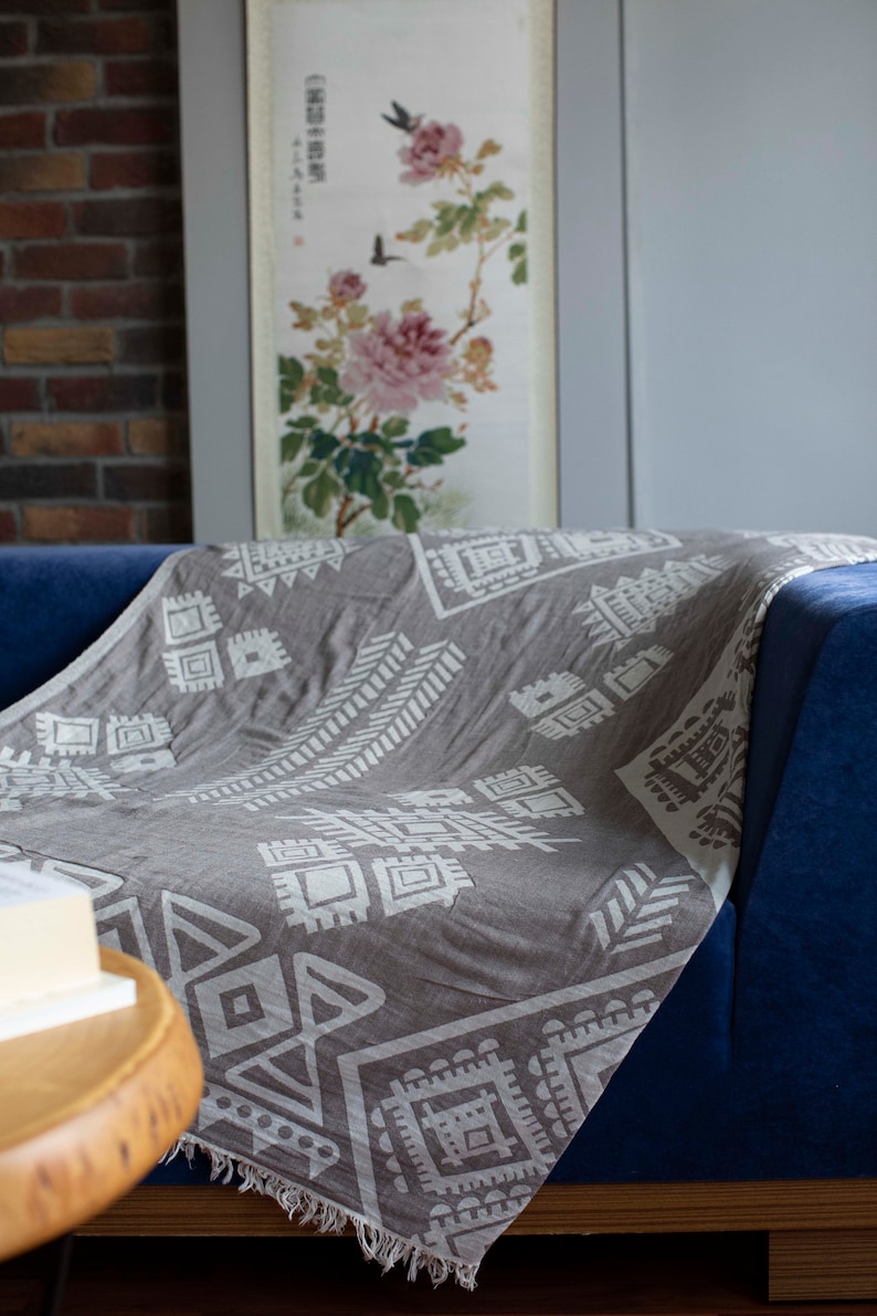 May include: A gray throw blanket with a white geometric pattern is draped over a blue couch. The blanket has a fringe border.