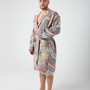 May include: A gray, pink, and yellow patterned bathrobe with a hood and a tie belt. The robe has a fringe trim.