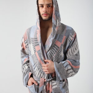 May include: A hooded robe with a geometric pattern in shades of blue, pink, and gray. The robe has a tie belt and two pockets.
