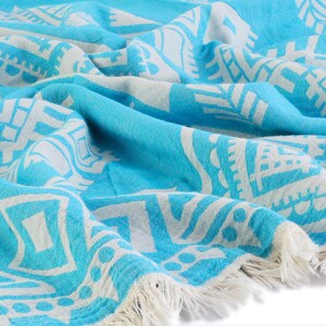 May include: A turquoise blue and white patterned Turkish towel with fringe. The towel is made of cotton and is soft and absorbent.