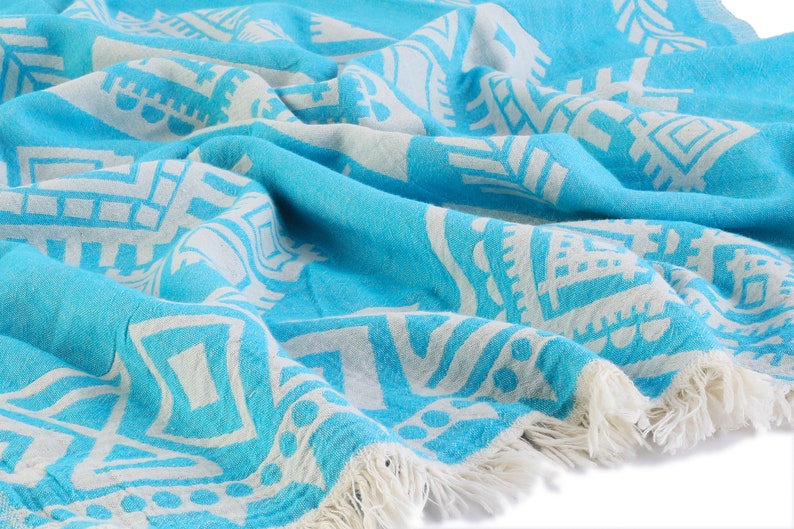 May include: A turquoise blue and white patterned Turkish towel with fringe. The towel is made of cotton and is soft and absorbent.