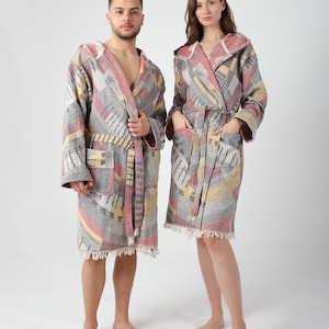 May include: Two hooded bathrobes with a geometric pattern in shades of gray, pink, and yellow. The robes have a tie belt and fringe trim.