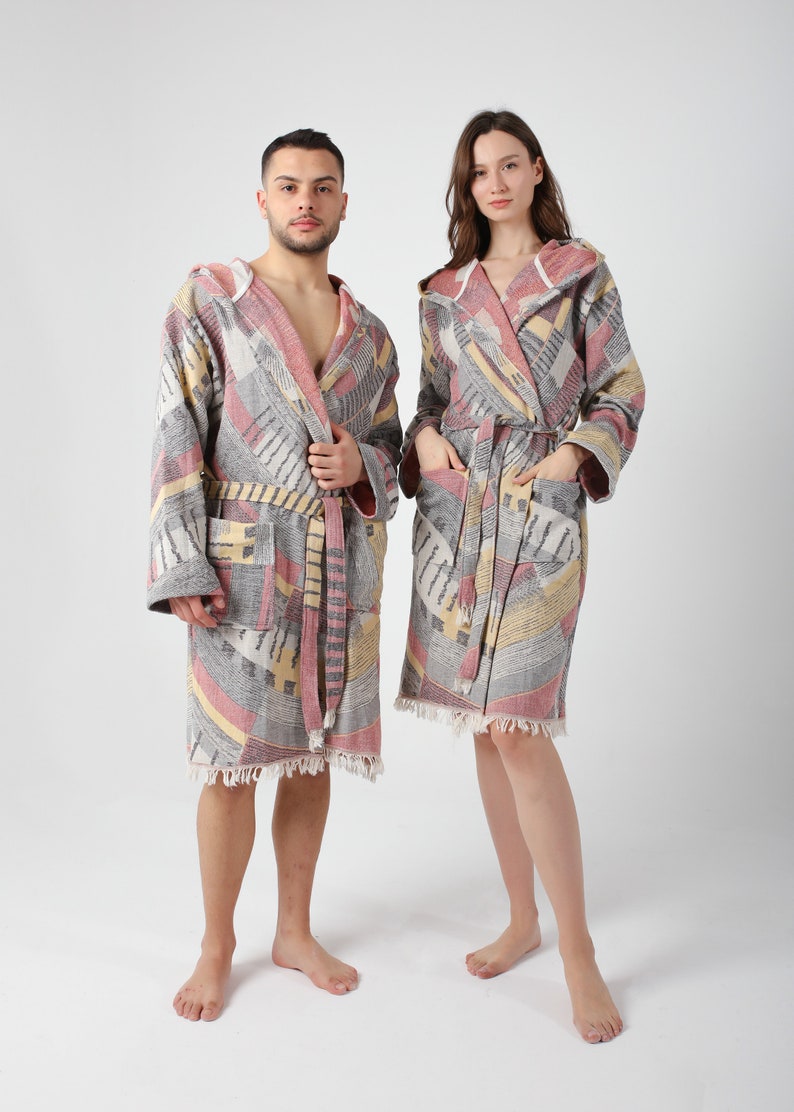 May include: Two hooded bathrobes with a geometric pattern in shades of gray, pink, and yellow. The robes have a tie belt and fringe trim.