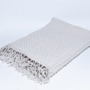 May include: A white waffle weave throw blanket with a fringe border. The blanket is folded in half and lying on a white surface.