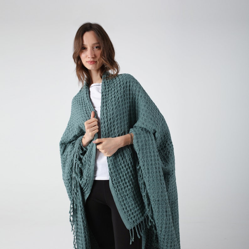 May include: A teal waffle weave throw blanket with fringe. The blanket is draped over a person's shoulders.
