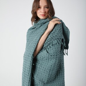 May include: A teal waffle weave throw blanket with fringe. The blanket is draped over a person's shoulders.