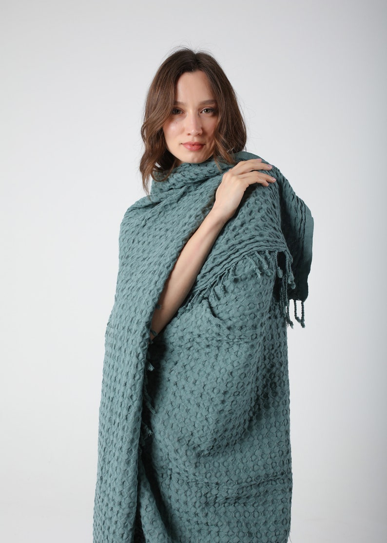 May include: A teal waffle weave throw blanket with fringe. The blanket is draped over a person's shoulders.