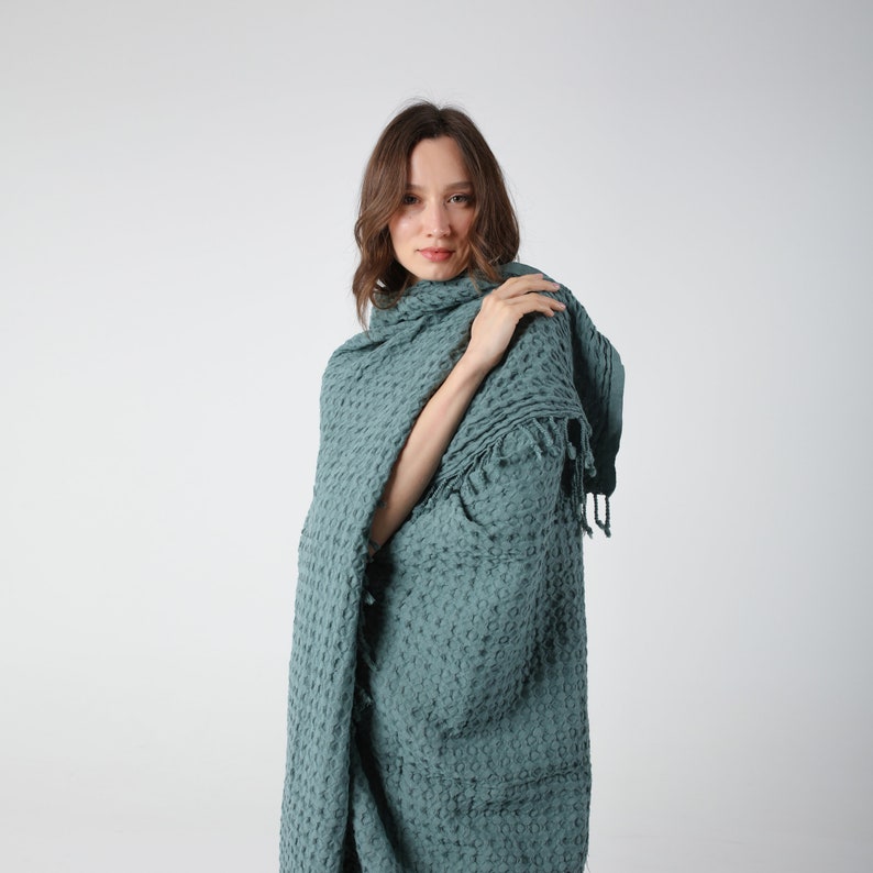 May include: A teal blue waffle weave throw blanket with fringe. The blanket is draped over a person's shoulders.