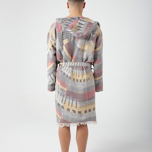 May include: A gray, pink, and yellow patterned robe with a hood and a belt. The robe has a fringed hem.