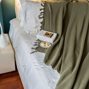 May include: A white bed with a green throw blanket and a book titled "Letters to a Young Poet" on top. The book is on a white plate with three cookies.