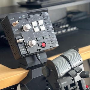 Könnte beinhalten: Schwarzes und graues Flugsimulator-Bedienfeld mit mehreren Knöpfen, Schaltern und Hebeln. Das Panel enthält einen Schubhebel und verschiedene Steuerflächen, die für eine realistische Flugsimulation konzipiert sind. Das Gerät ist auf einem Schreibtisch montiert.