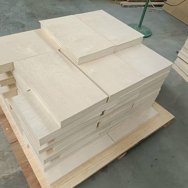 May include: A stack of light wood panels, probably plywood, are stacked on a wooden pallet. The panels are smooth and have a light wood grain.