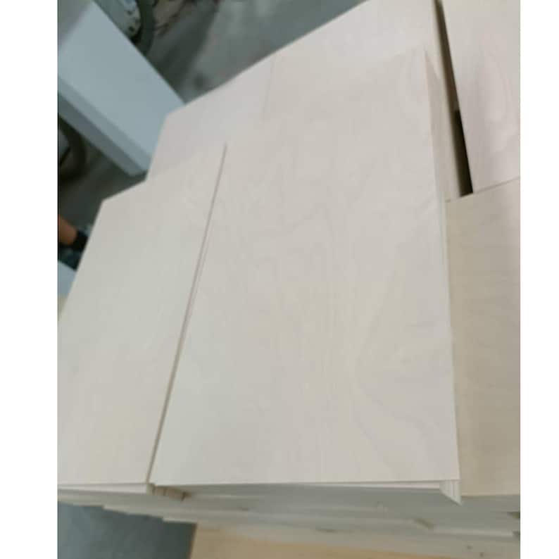 May include: Stack of light-coloured wood panels, probably plywood, with a smooth, slightly textured surface.